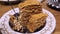 A multi-layered sweet cake in a plate on the table is eaten with a spoon