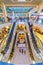 multi-level network of escalators in the Trade House `Aurora Mall`. The citizens walk, rest and make purchases. Text in Russian: