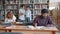 Multi-racial group of students studying in library with books reading talking