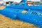 A multi-row toothed metal harrow of blue color against the background of a harvested yellow field, close-up