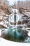 Multi tiered waterfall cascading down rocks in a snowy winter wonderland scene.