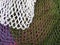 The multicolor background of the zero waste string bags, closeup of the knitted net. Selective focus