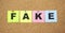 Multicolor notes with letters pinned on a cork board. Word FAKE