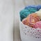 Multicolored cotton yarn in basket on white wooden background
