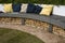 Multicolored cushions in the garden on a long round bench of modern material