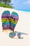 Multicolored flip-flops and sunglasses on a sunny beach..Tropical beach vacation and travel concept, vertical composition