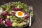 Multicolored leafy vegetables mix, chickpeas, mung bean, egg and fork in black plate