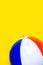 Multicolored striped inflatable beach ball on bright yellow background. Summer sports vacation beach kids fun travel