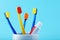 Multicolored toothbrushes and a toothpaste tube in a holder cup against blue background