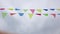 Multicolored triangular flags hang on a string and flutter in the wind against a cloudy cloudy sky