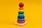 Multicolored wooden toy pyramid on yellow background. Toy, build from colored wooden rings