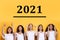 Multicultural Ladies Pointing Fingers At Number 2021 Above Head, Yellow Background