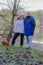 Multicultural mature married couple smiling at camera by a lake, wearing winter clothes