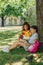 Multicultural schoolgirls reading books while sitting on lawn under tree