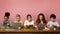 Multiethnic children with electronic devices and books studying at table over pink background, free space