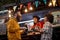 Multiethnic couple eating sandwiches in front of fast food service, laughing, socializing with employee, talking