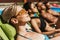multiethnic friends in sunglasses sunbathing on sunbeds at poolside