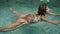 Multiethnic woman swims gracefully in clear water of pool, hair flows. Female enjoys leisure swim, relaxes in