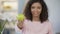 Multiethnic young woman offering apple, smiling at camera, healthy lifestyle