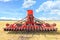 A multifunctional agricultural harrow stands in a harvested wheat field against a blue cloudy sky on a summer day