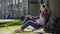 Multinational young woman in headphones sitting under tree, listening to music