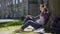 Multinational young woman in headphones sitting under tree, listening to music