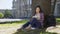 Multinational young woman taking notes in notebook sitting under tree, essay