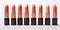 Multiple different shades of peach fuzz color lipstick in a black case in a row on a white background. Make up a product