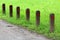 Multiple small wooden poles with reflective red dots put in a row next to gravel path surrounded with uncut grass in local park