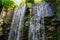 Multiple waterfalls streaming of a big rock cliff in a forest, nature background