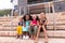 Multiracial cheerful elementary schoolgirls sitting on steps against school building
