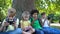 Multiracial children company playing games on gadgets sitting under tree in park