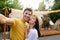 Multiracial couple in love taking selfie at campsite, resting with friends near RV, spending summer weekend outdoors