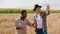 Multiracial farmers in the middle of wheat field using the laptop to analyse the statistics of harvest from this year