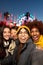 Multiracial friends having fun together taking vertical selfie during winter market at night looking at camera.