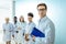 Multiracial group of smiling medical interns in lab coats standing in a row with clipboards
