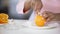 Multiracial lady cutting orange with knife on plate, healthy dieting, vitamins