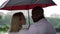 Multiracial loving couple is standing under umbrella in rainy day and kissing