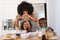 Multiracial mother with afro hair breaking egg with daughter in bowl while making breakfast on table