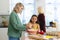 Multiracial mother and daughter whisking batter in bowl while senior woman looking through window