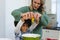 Multiracial mother making face while assisting son with afro hair in breaking egg in bowl in kitchen