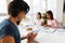 Multiracial sisters doing puzzle while their mother using cellphone