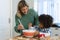 Multiracial smiling mother with son whisking batter in bowl on wooden table in kitchen