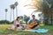 Multiracial teenagers playing guitar while sitting on green lawn in park and enjoying summer day together.