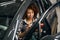 Multiracial woman auto mechanic sits in a car with device