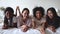 Multiracial women friends wear pyjamas looking at camera on bed