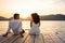 Multiracial young couple caucasian and hispanic sitting on a jetty with two red wine glasses and setting sunlight between them -