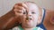 Mum feeds the beautiful baby with a spoon fruit porridge. The child looks at one point carefully. Close-up