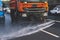 Municipal watering truck machines washes asphalt, process of street disinfection and cleaning from dust and dirt, cleaning flusher