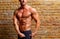 Muscle shaped man posing on gym brick wall